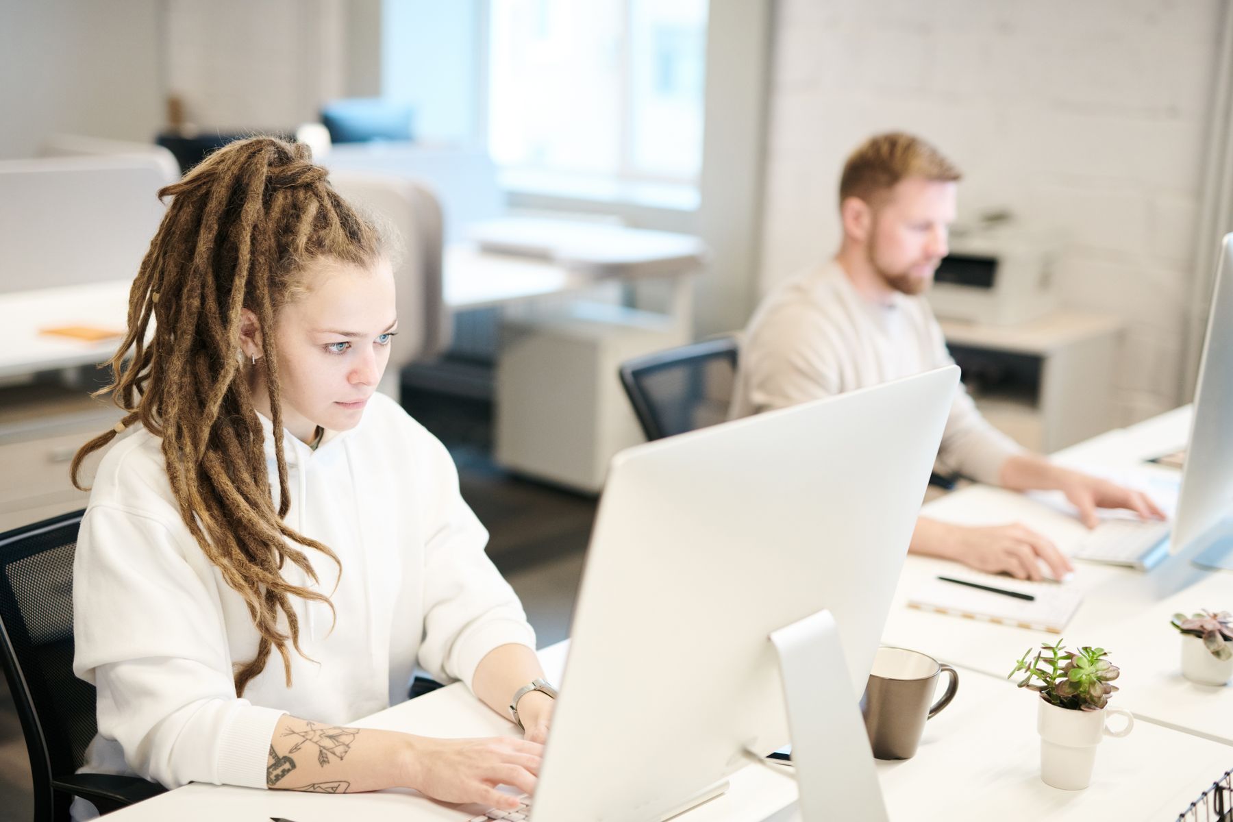 Two people working at computers in a bright shared workplace